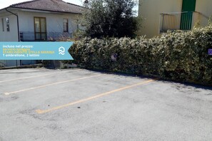 A parking lot with a building in the background, a hedge, and a sign with text. - N148 - Numana, new three-room apartment with terrace 350mt from the sea (Numana)