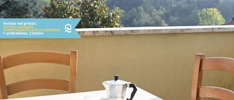 A table with a teapot and cups, a mat, and some snacks on a balcony overlooking a forested area.