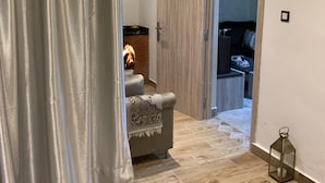 Una habitación con suelo de madera, un sofá con una manta estampada, una puerta de madera y una chimenea encendida.