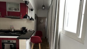 Una cocina estrecha con una isla central, armarios rojos, horno empotrado y una ventana con cortinas.