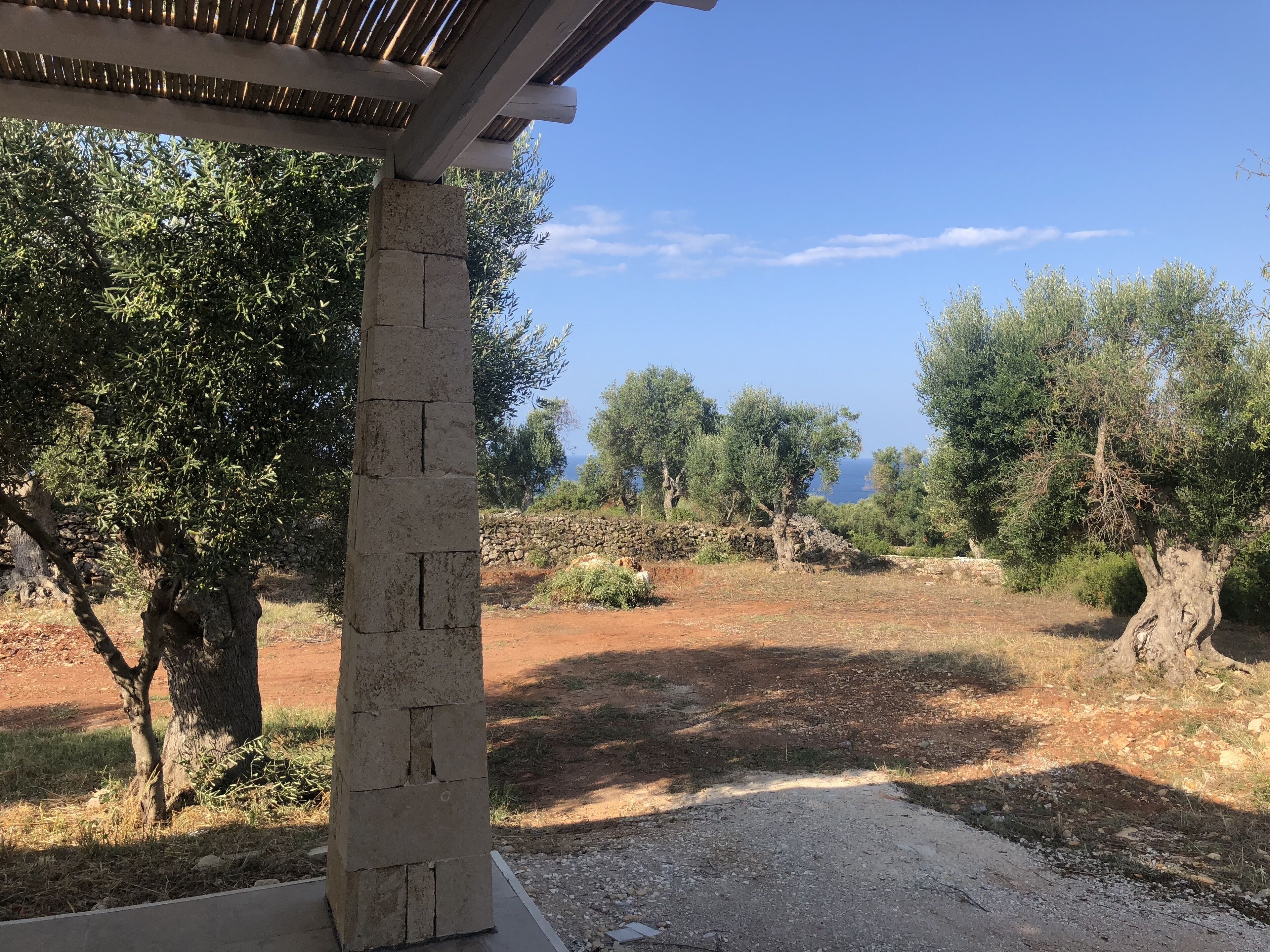 A stone pillar in a rustic outdoor setting with olive trees and a stone wall in the background.