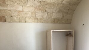 A single bed with a wooden frame and white bedding in a room with a stone wall and a wooden bench.