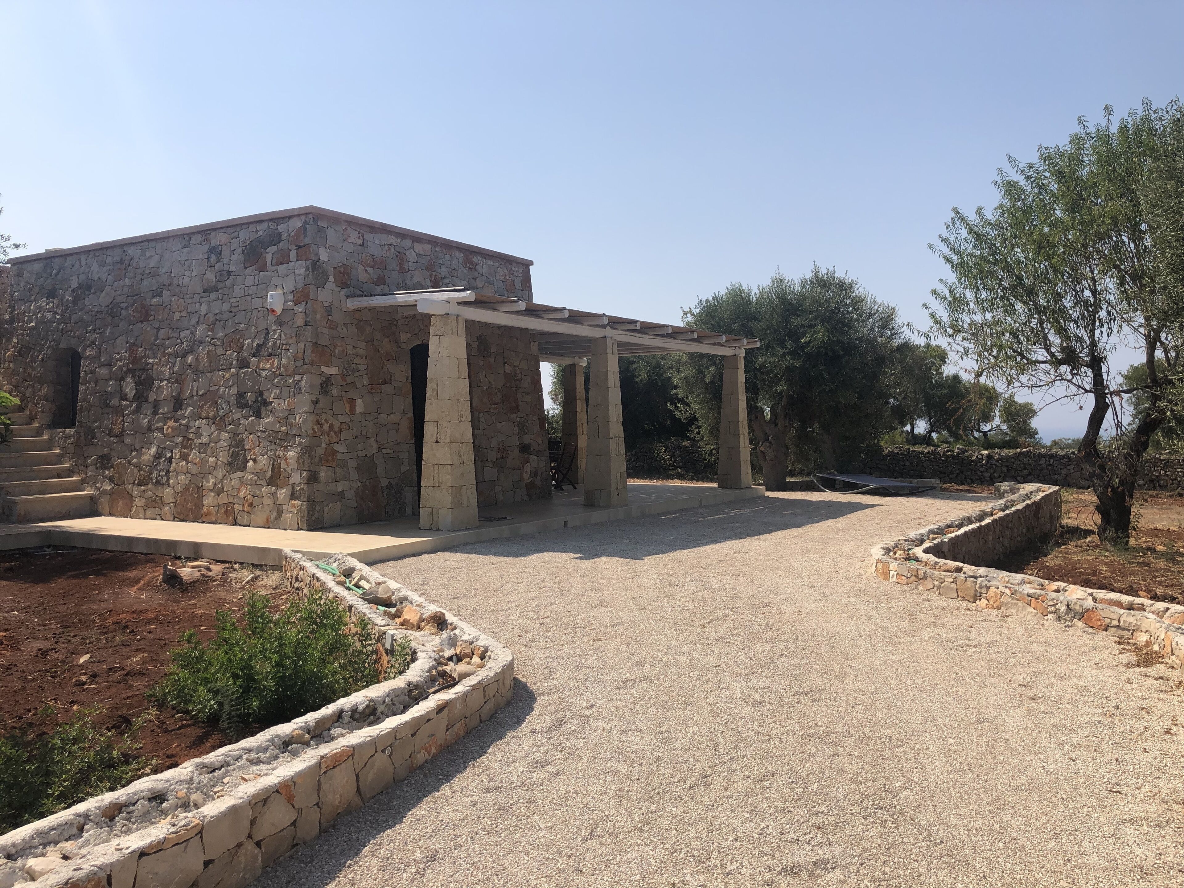 A stone building with a covered outdoor area, gravel paths, and surrounding vegetation.