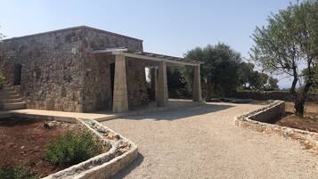 A stone building with a covered outdoor area, gravel paths, and surrounding vegetation.