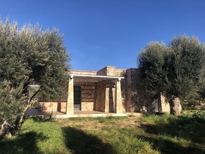A stone building with a covered entrance and columns, surrounded by olive trees and grass. - SAN GREGORIO VILLA WITH SECULAR OLIVE GROVE, GARDEN AND PORCH (Patù)