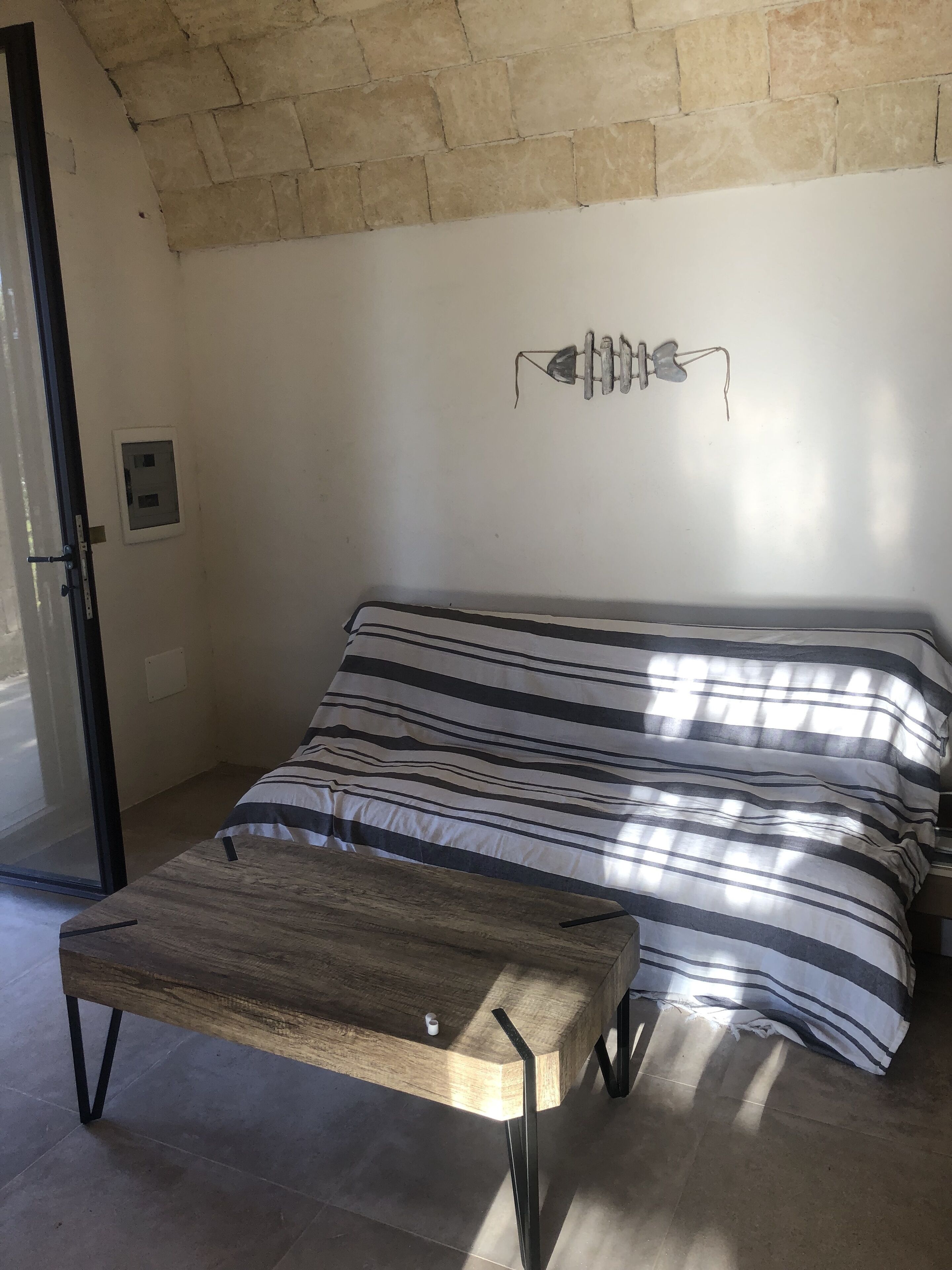 A room with a bed, a wooden table, a wall socket, and a window.