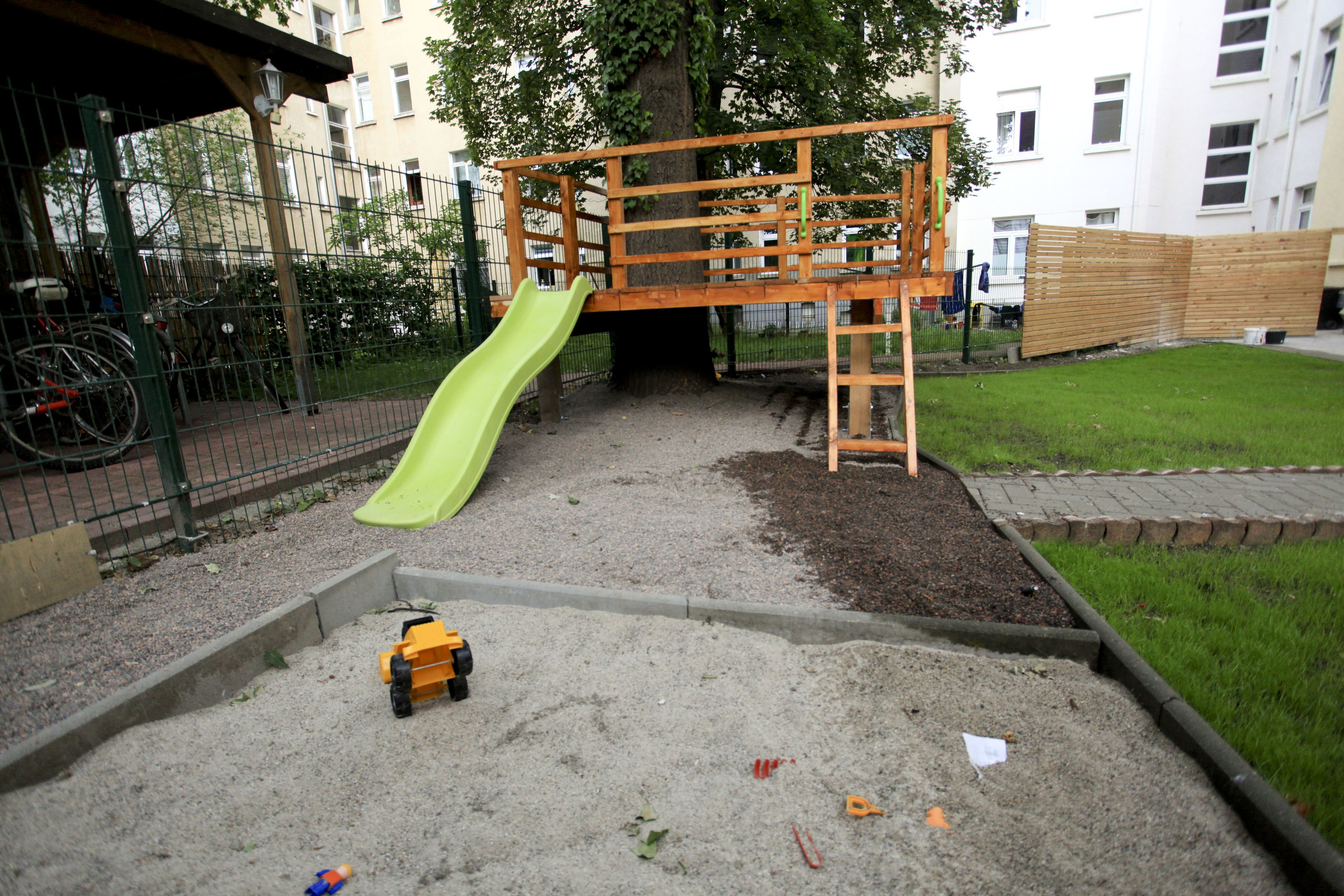 Un parque infantil con tobogán, zona de arena y estructura de madera para escalar.