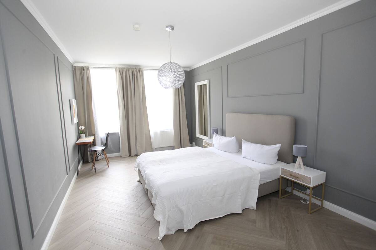 Un dormitorio moderno con una cama grande, mesitas de noche, un escritorio y una silla.