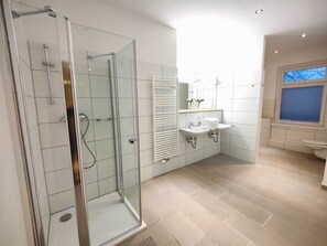 Un baño moderno con ducha de vidrio, tocador con lavamanos y espejo, y ventana que proporciona luz natural.