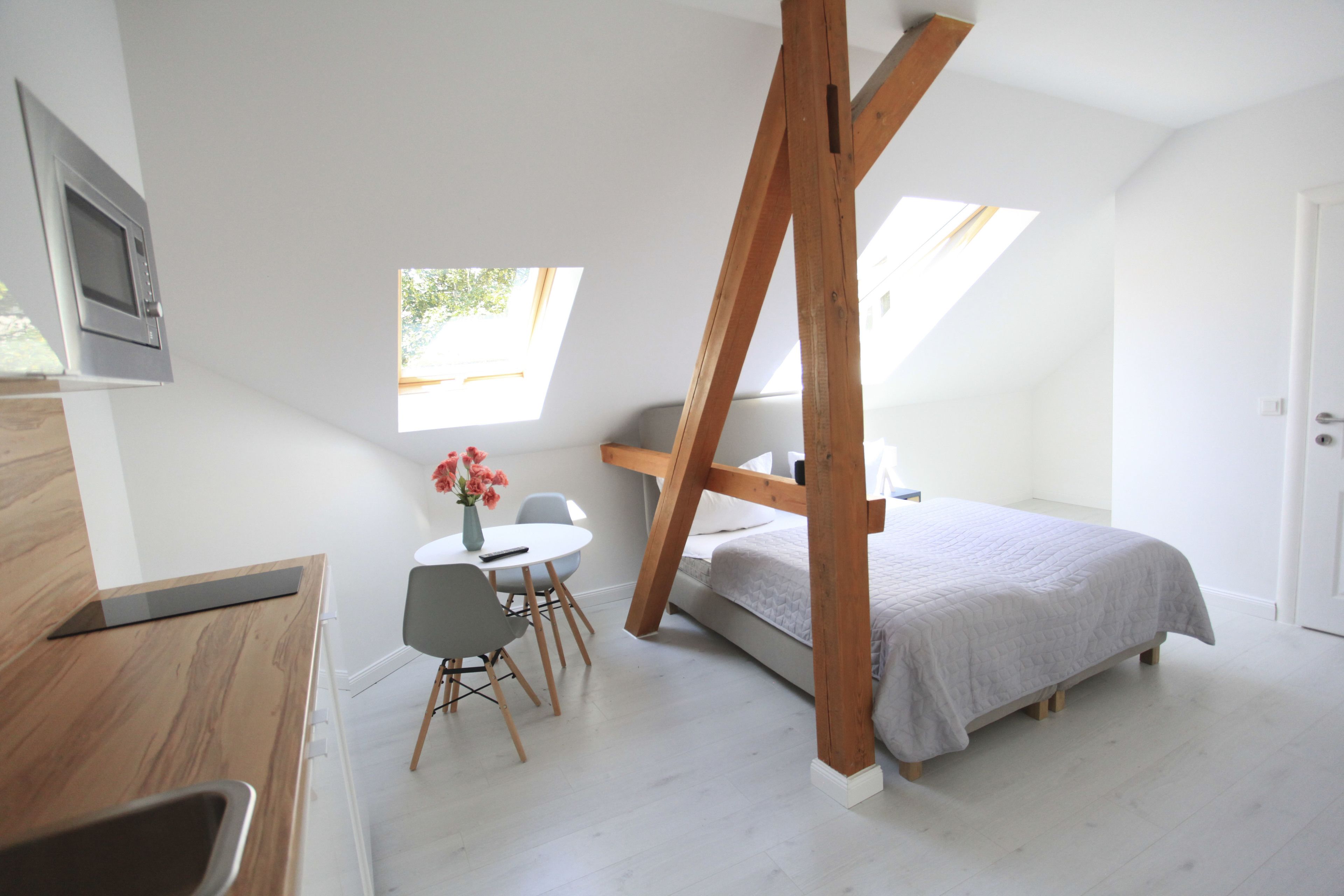 Une chambre à coucher de taille modeste, comprenant un lit, une petite table avec des chaises, une fenêtre et une poutre en bois au plafond.
