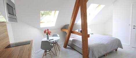 Une chambre à coucher de taille modeste, comprenant un lit, une petite table avec des chaises, une fenêtre et une poutre en bois au plafond.