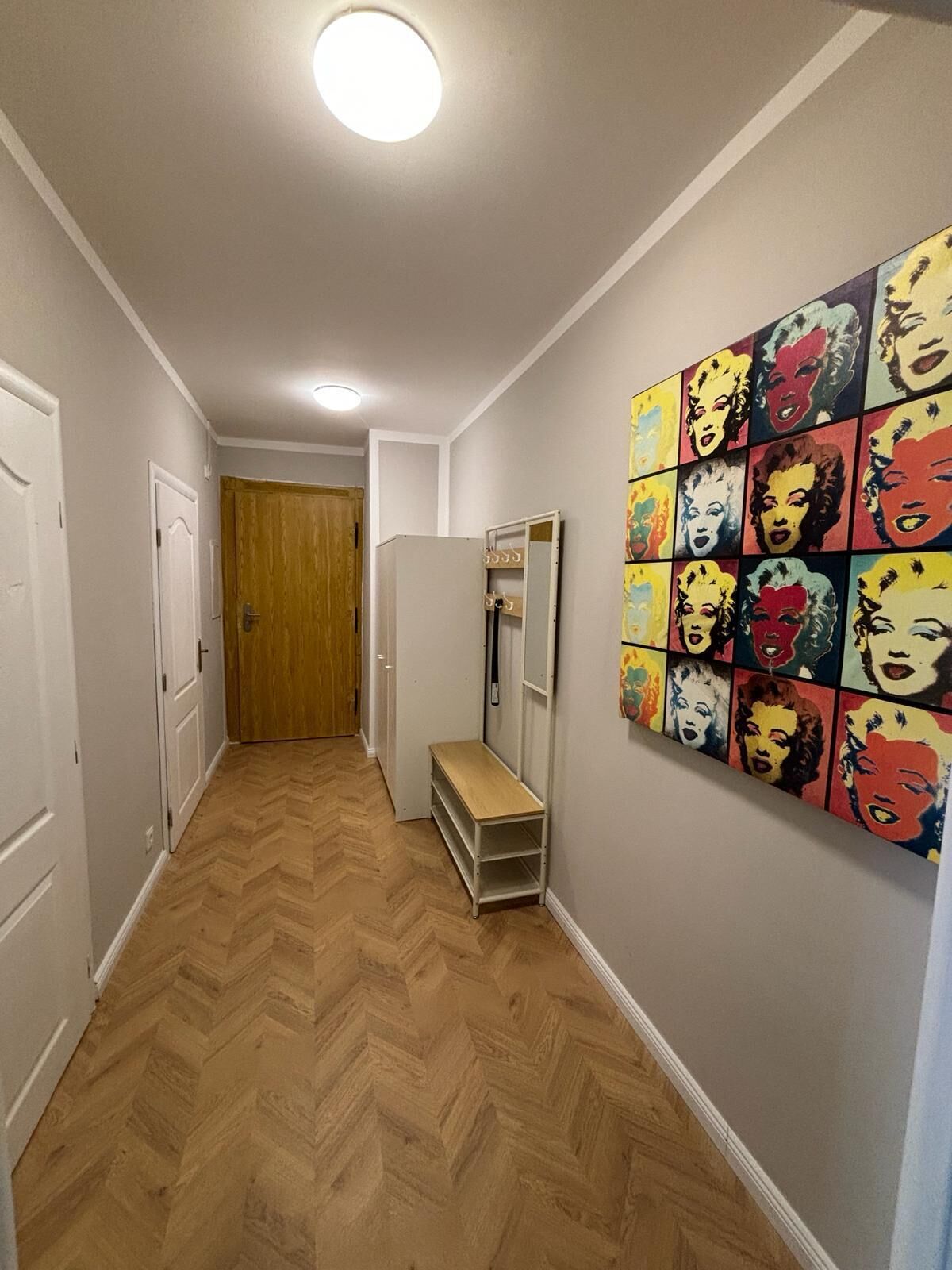 A hallway with a herringbone floor, a wooden door at the end, and a colorful pop art mural on the wall.
