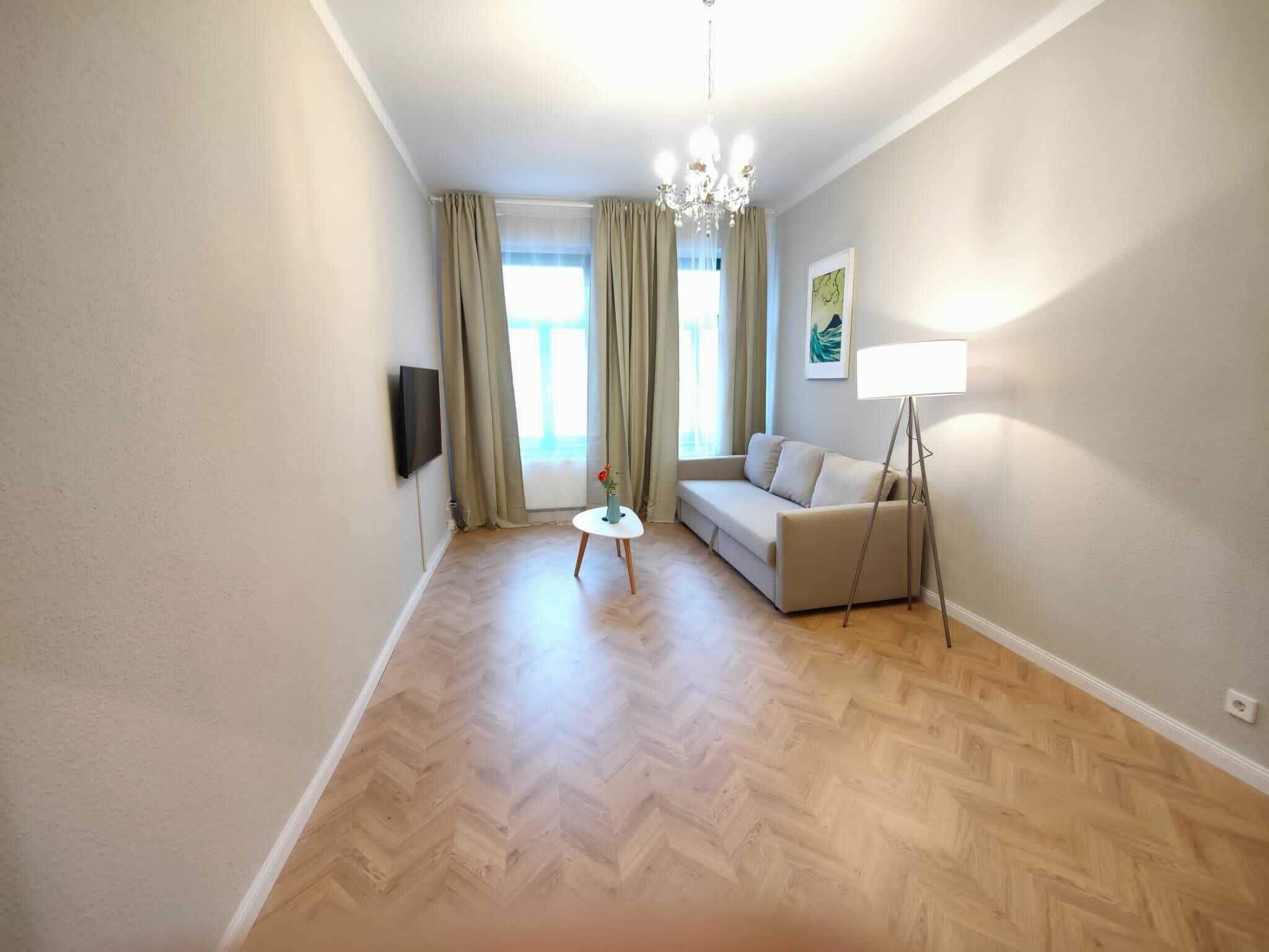 Un salon moderne avec un canapé, une petite table sur laquelle est posé un vase, une lampe sur pied et un téléviseur fixé au mur.