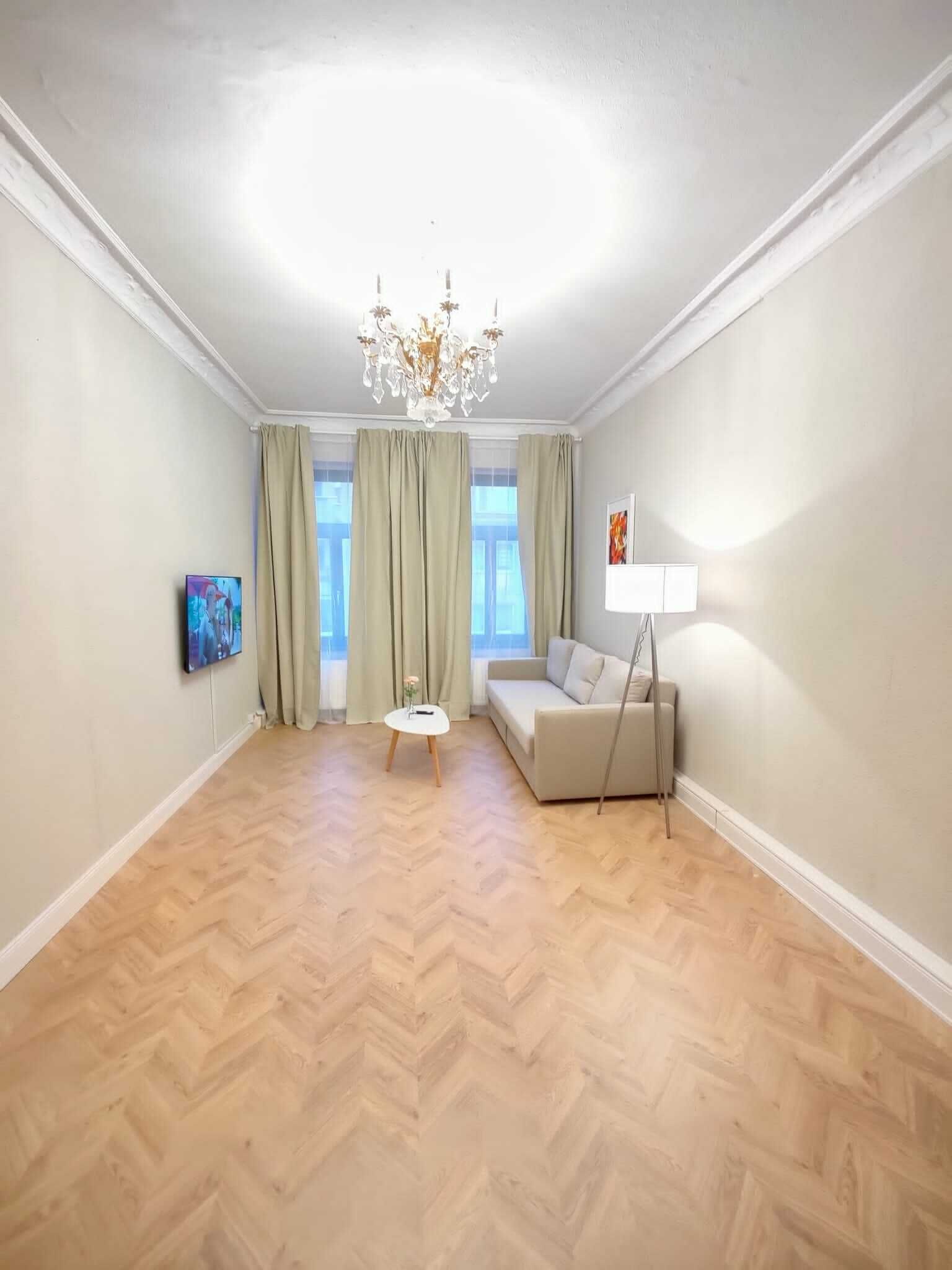 Un ampio soggiorno con parquet a spina di pesce, un divano, un tavolino, una televisione e un lampadario.