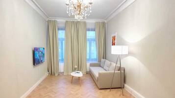 Un ampio soggiorno con parquet a spina di pesce, un divano, un tavolino, una televisione e un lampadario.
