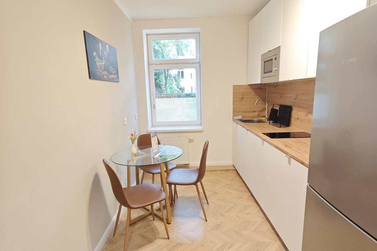 Una cocina compacta con zona de comedor, una ventana con persianas, un microondas Bosch y un refrigerador.