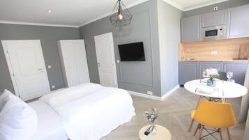 Een moderne hotelkamer met een groot bed, een klein rond tafeltje met een bloevas, een aan de muur bevestigde televisie en een kitchenette.