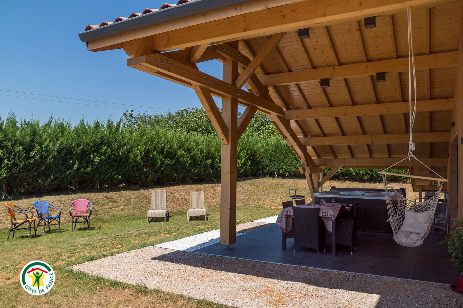 Un espacio al aire libre cubierto con una mesa, sillas y una hamaca colgante, con vista a un área boscosa.