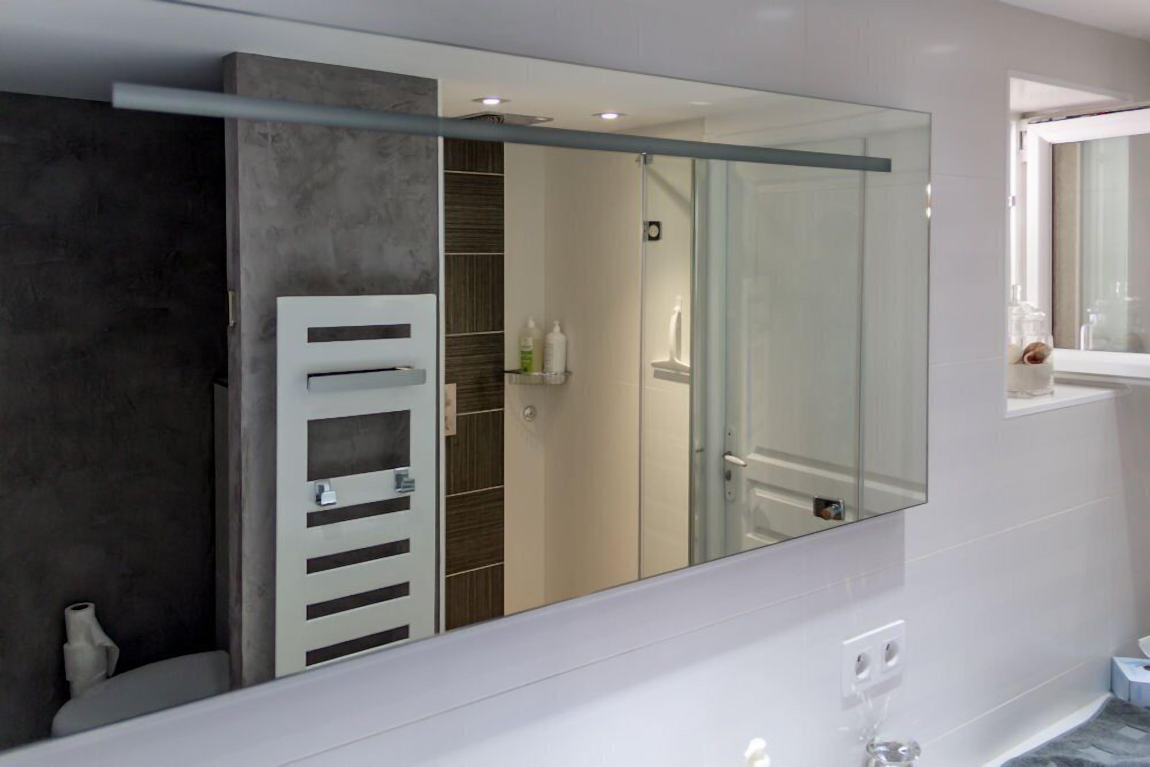 A modern bathroom with a large mirror, a glass shower enclosure, and a white towel rack.