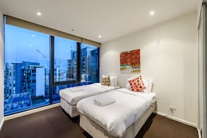 Enjoy city views from the large window, featuring two single beds with crisp linens and a unique painting above.