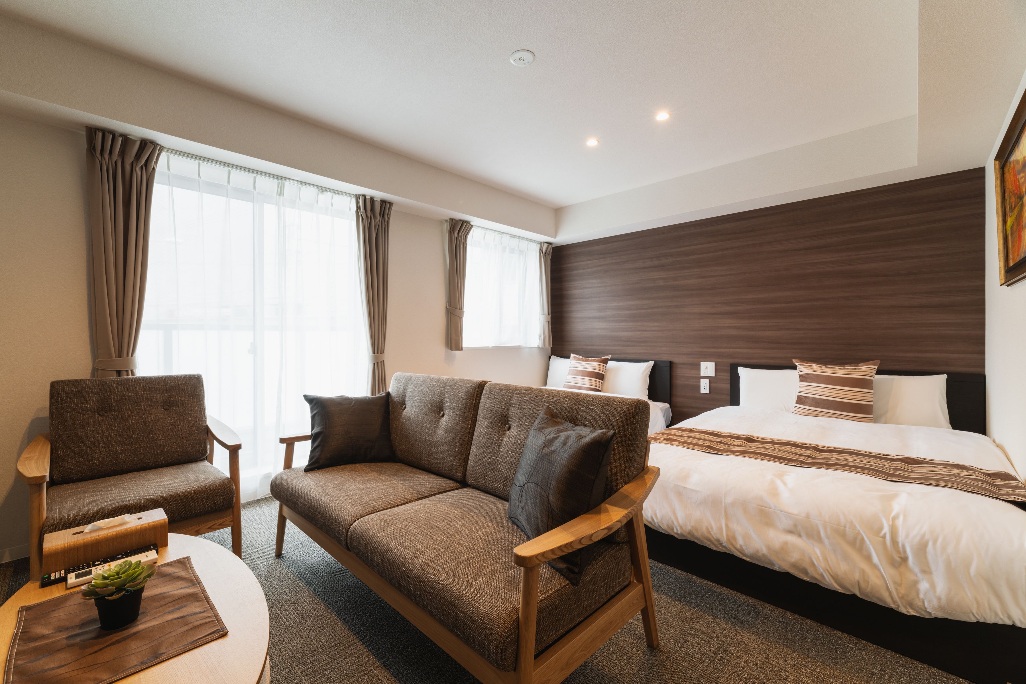 Une chambre d’hôtel avec un canapé, un fauteuil et un lit doté d’une tête de lit en bois.