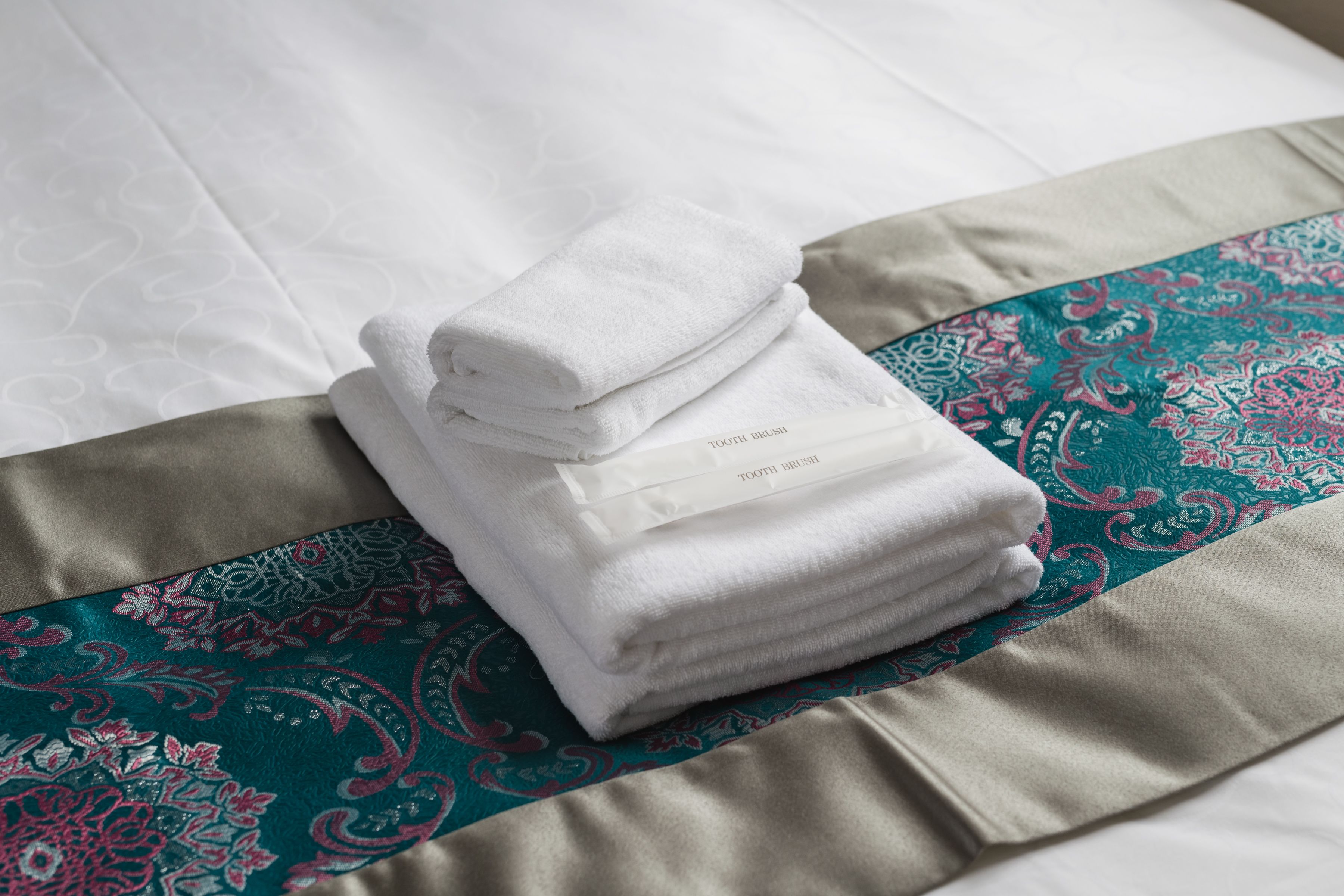 A neatly folded white towel with a label on a bed with patterned bedding.