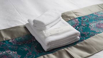 A neatly folded white towel with a label on a bed with patterned bedding.
