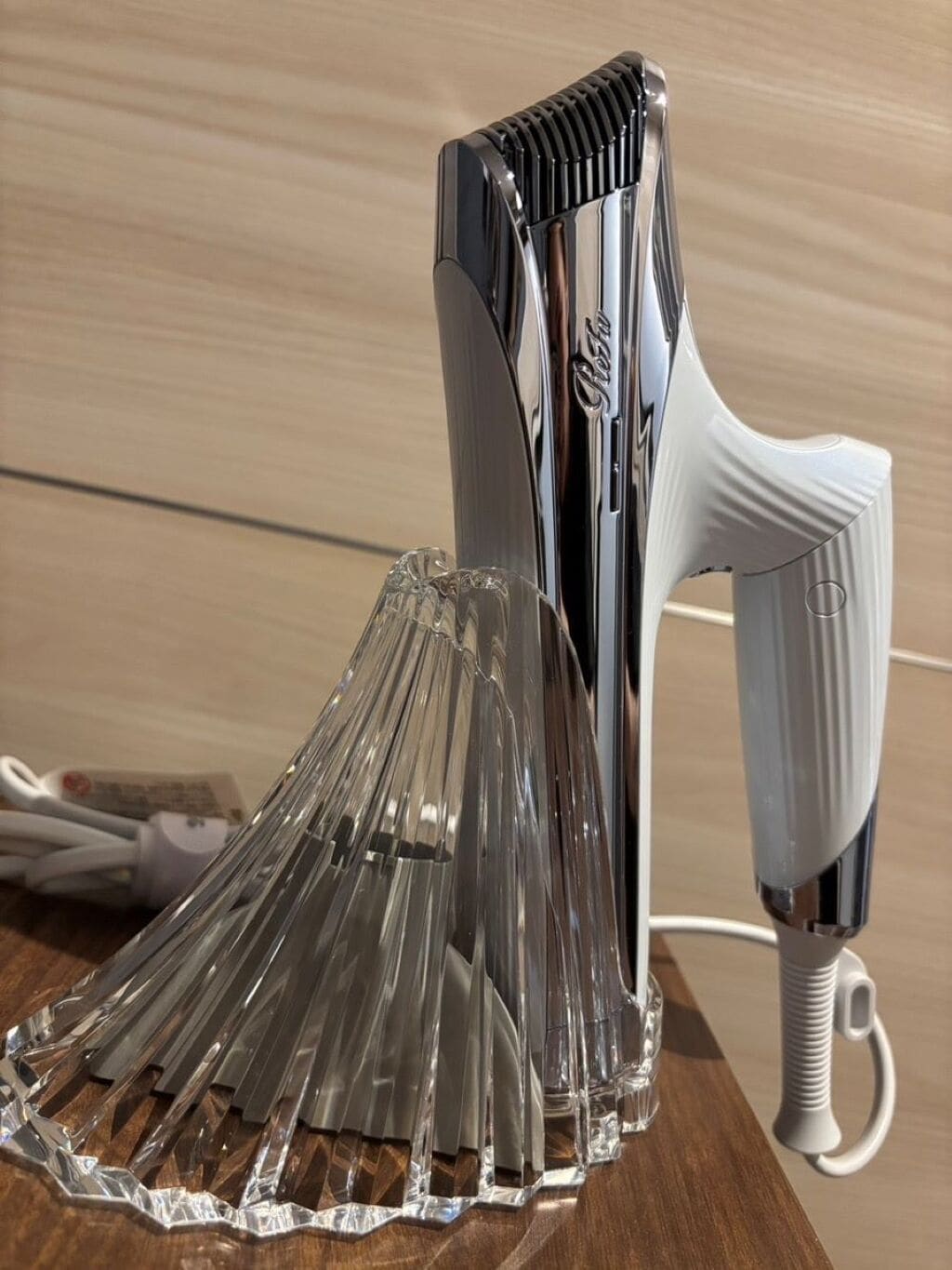 A chrome hair dryer and a clear glass carafe on a wooden surface.