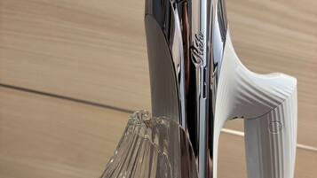 A chrome hair dryer and a clear glass carafe on a wooden surface.