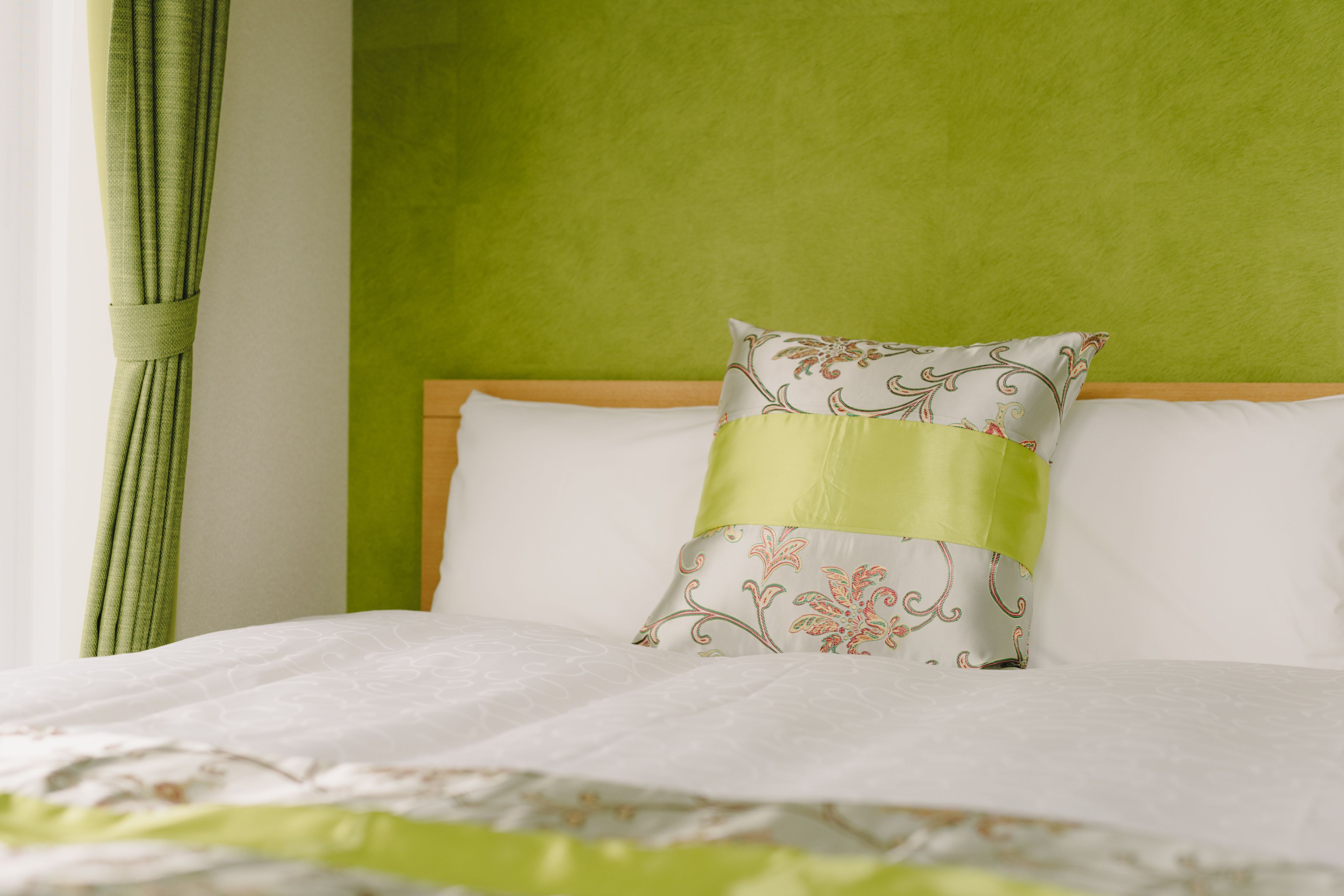 A bed with a green headboard, a white pillow with a floral pattern, and a green curtain.