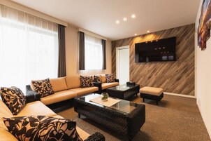 Una sala moderna con un conjunto de sofás, una mesa de centro de vidrio y un televisor de pantalla plana montado en una pared de madera.