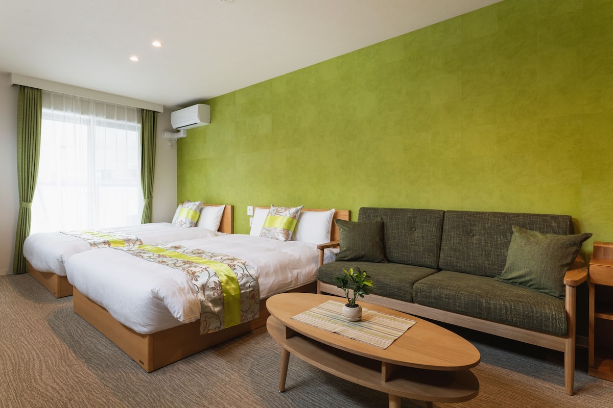 A hotel room with a bed, a sofa, a coffee table, and a green wall.
