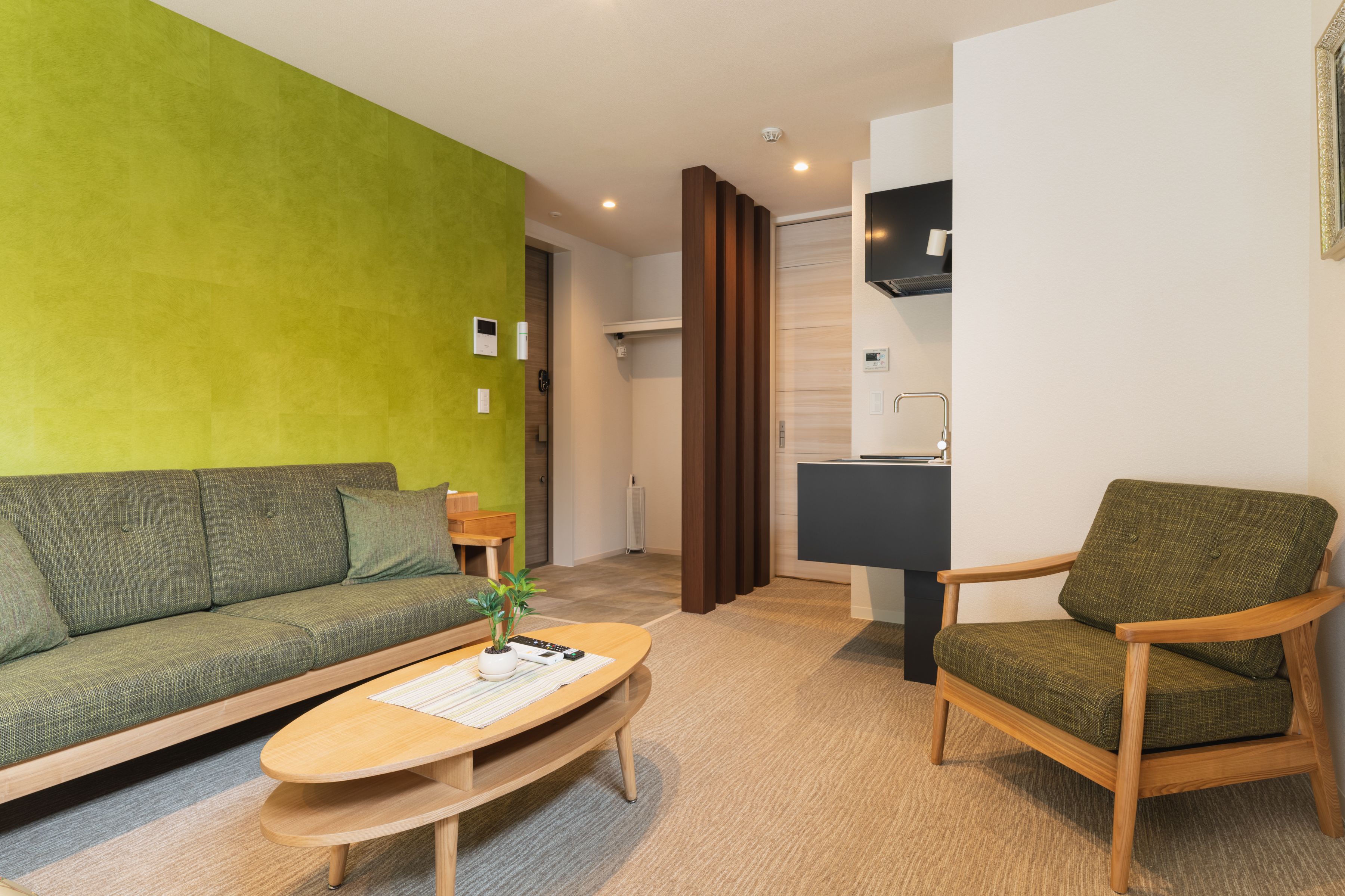 A modern living room with a green wall, a sofa, a wooden coffee table, and a green armchair.