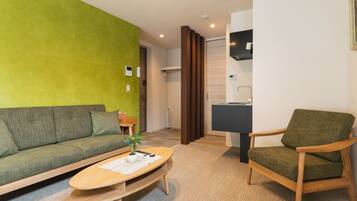 A modern living room with a green wall, a sofa, a wooden coffee table, and a green armchair.