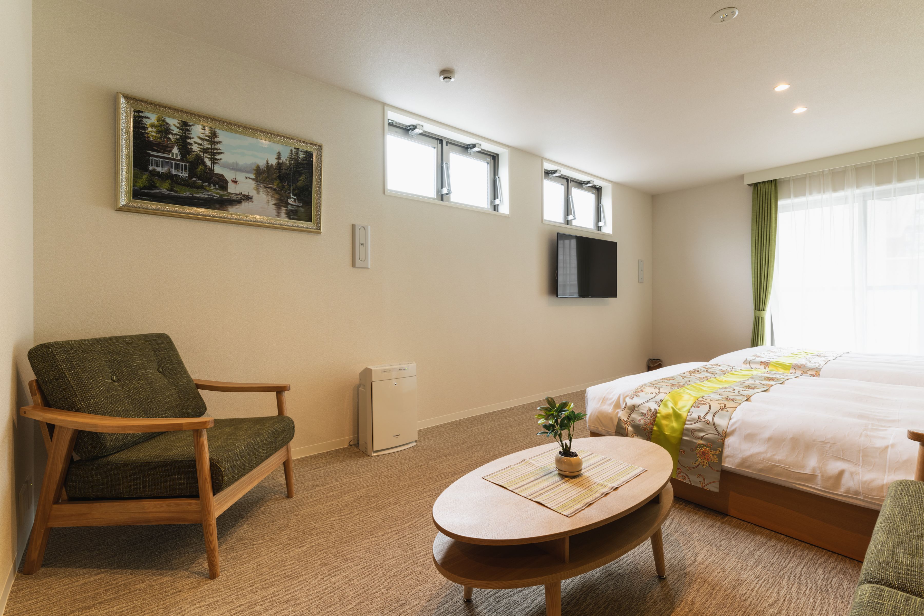 A hotel room with a bed, a chair, a small table, a painting on the wall, and a window.