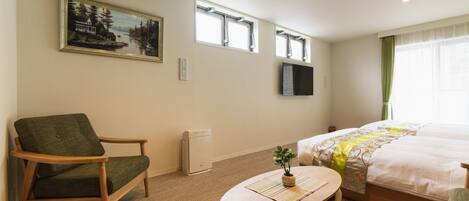 A hotel room with a bed, a chair, a small table, a painting on the wall, and a window.