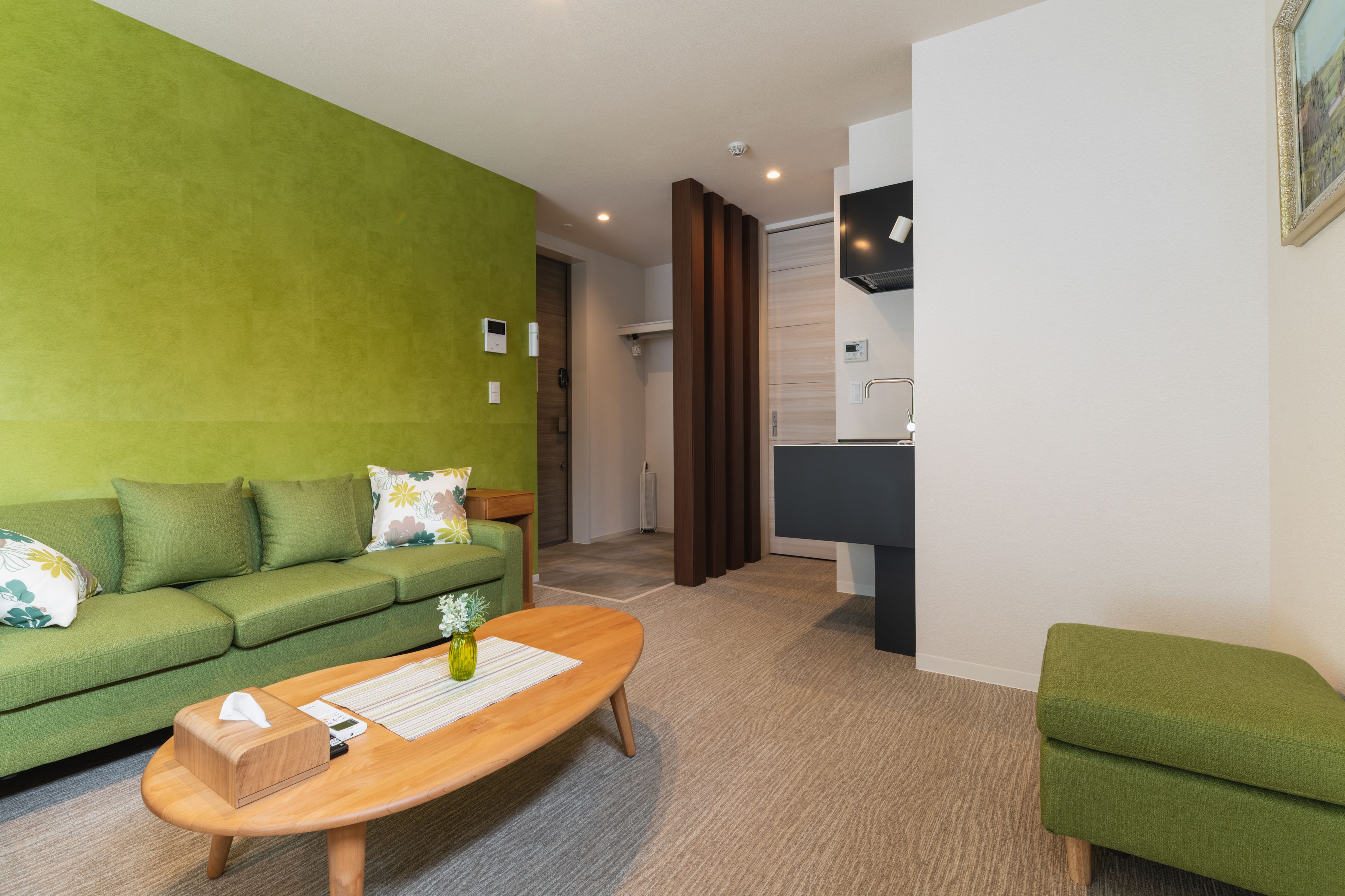 A modern living room with a green sofa, a wooden coffee table, and a small green ottoman.