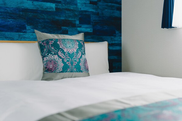 Una cama con sábana blanca y almohada decorativa de estampado paisley.