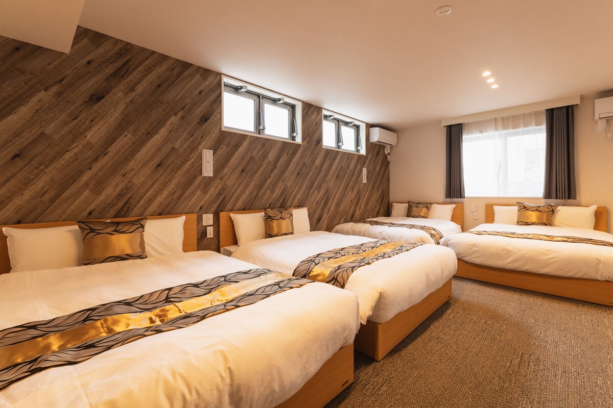 A hotel room with three beds arranged in a row, wooden wall paneling, and a large window with curtains.