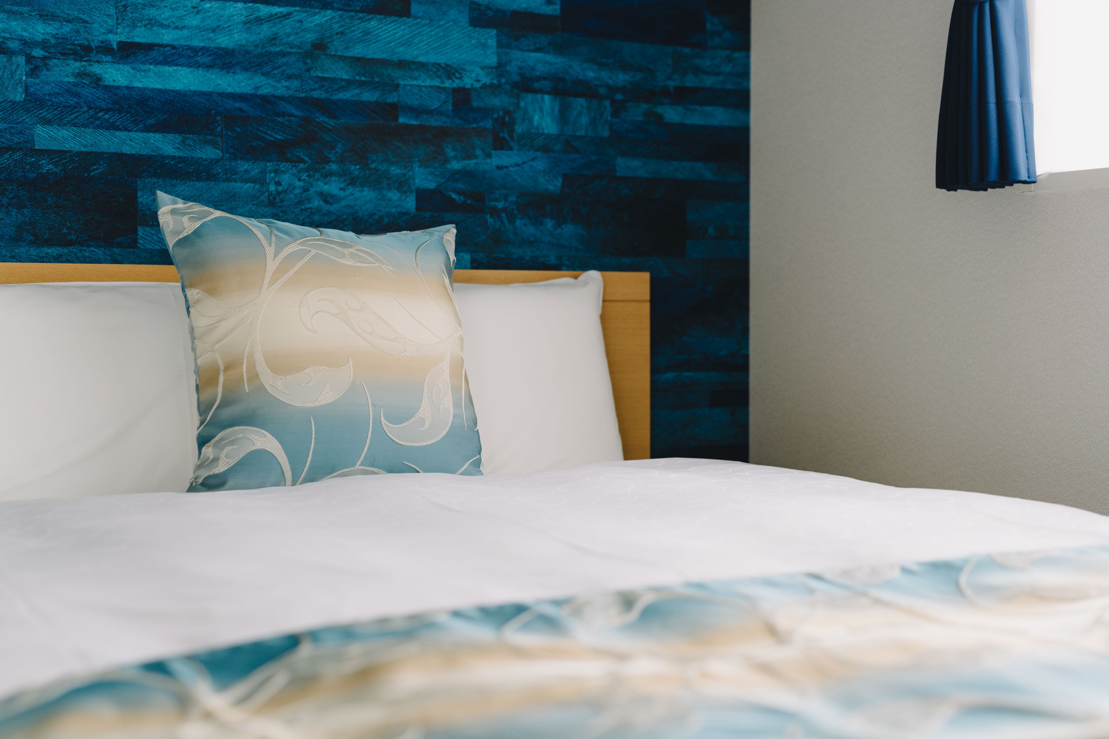 A bed with white bedding and a decorative pillow against a wooden headboard.