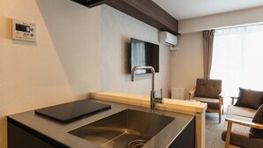 A modern hotel room with a built-in kitchen, a flat-screen TV mounted on the wall, and a seating area with a sofa and armchairs. - GRAND BASE Mojiko (Kitakyushu)