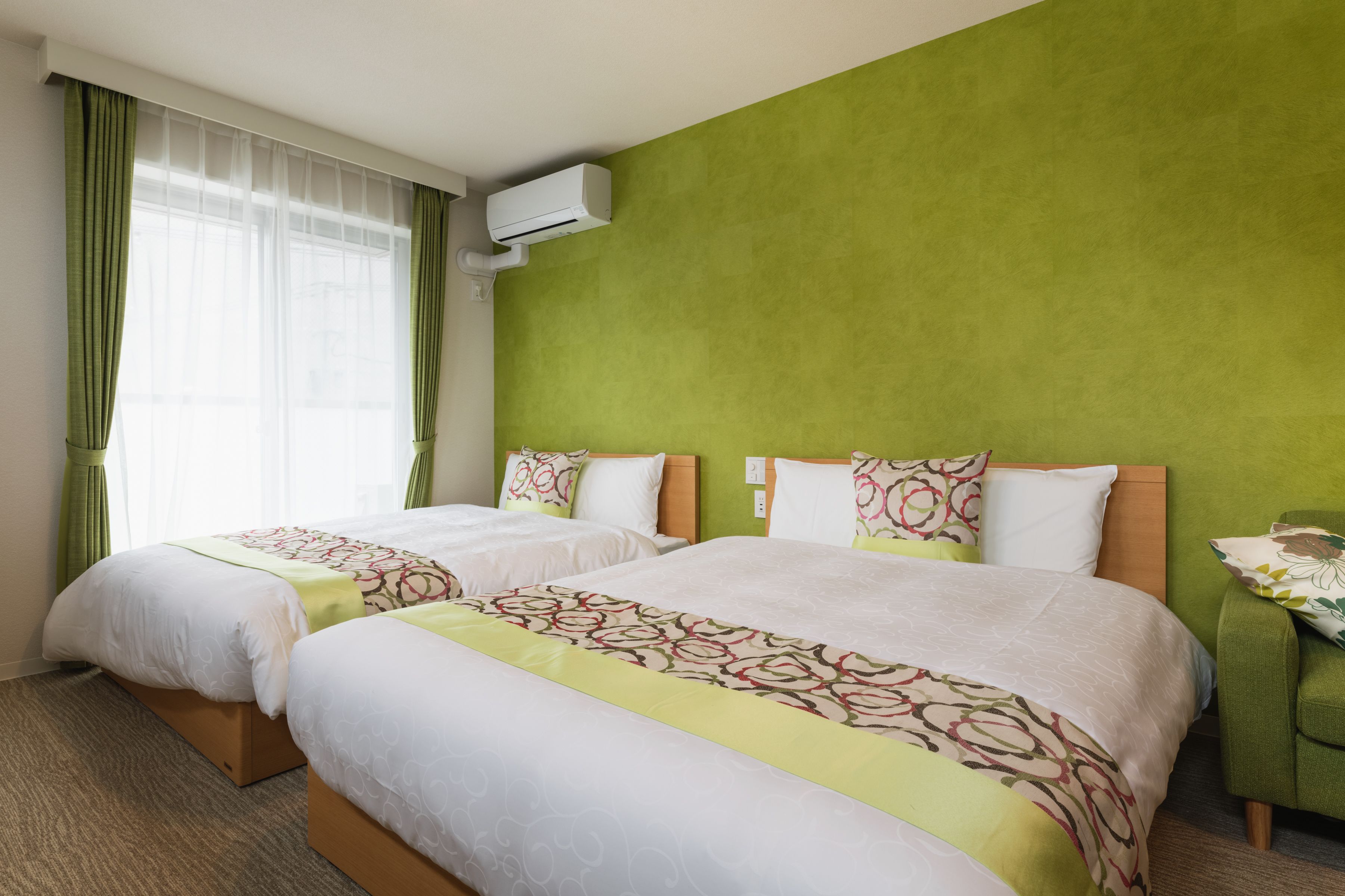 Quarto de hotel com duas camas, paredes verdes e um aparelho de ar condicionado.