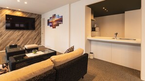A modern living room with a flat-screen TV, a coffee table, a sofa, and a kitchen area with a sink and cabinets. - GRAND BASE Mojiko (Kitakyushu)