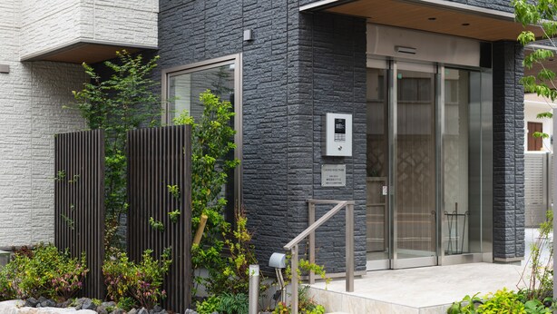 A modern building with a stone facade, large glass doors, and a small outdoor area with plants and a metal mailbox. - GRAND BASE Mojiko (Kitakyushu)