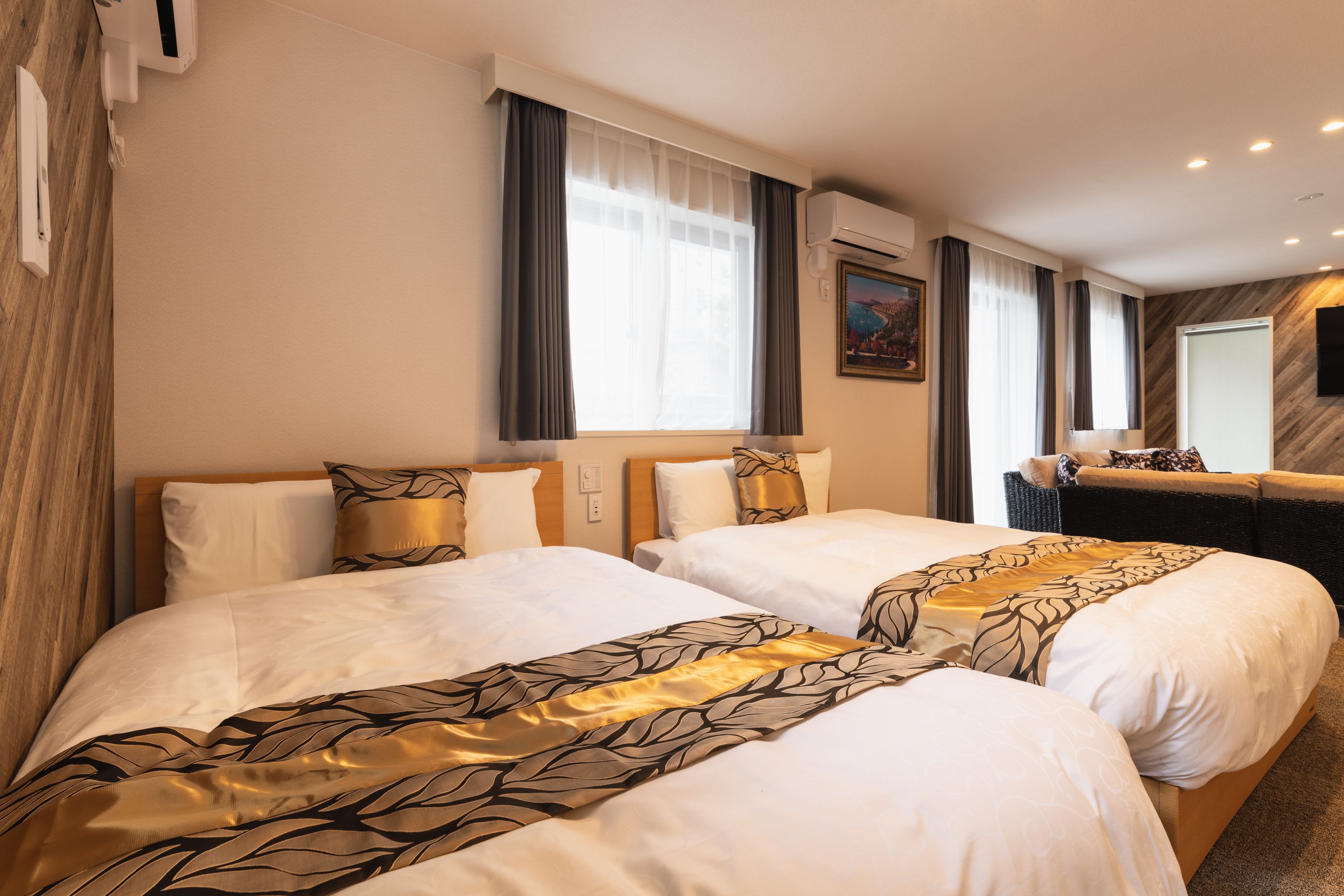 A hotel room with two beds, a sofa, a painting on the wall, and an air conditioning unit.
