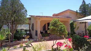 A two-story house with a covered patio, surrounded by lush greenery and flowering plants. - B&B Eden di Segesta (Calatafimi)