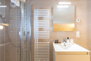 Um banheiro moderno com box de vidro, porta-toalhas branco, espelho grande e pia com artigos de higiene pessoal.