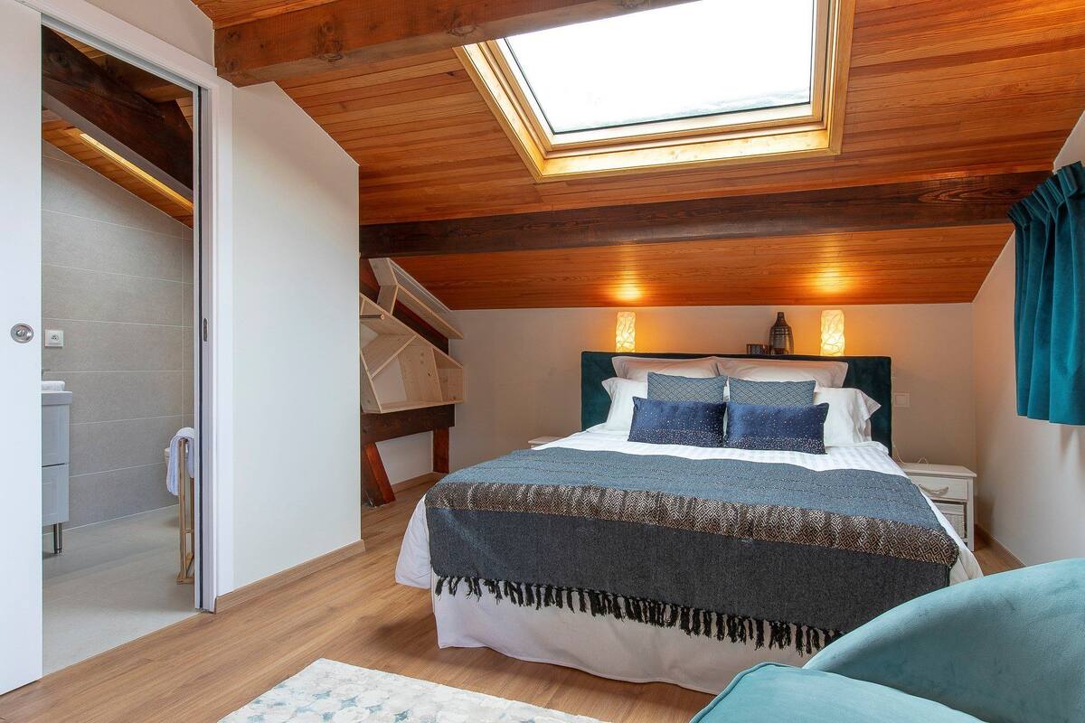 A bedroom with a skylight, wooden ceiling, and a bed with patterned bedding.