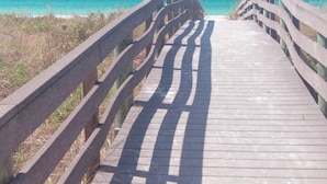 A wooden boardwalk leading to a beach with clear blue water.