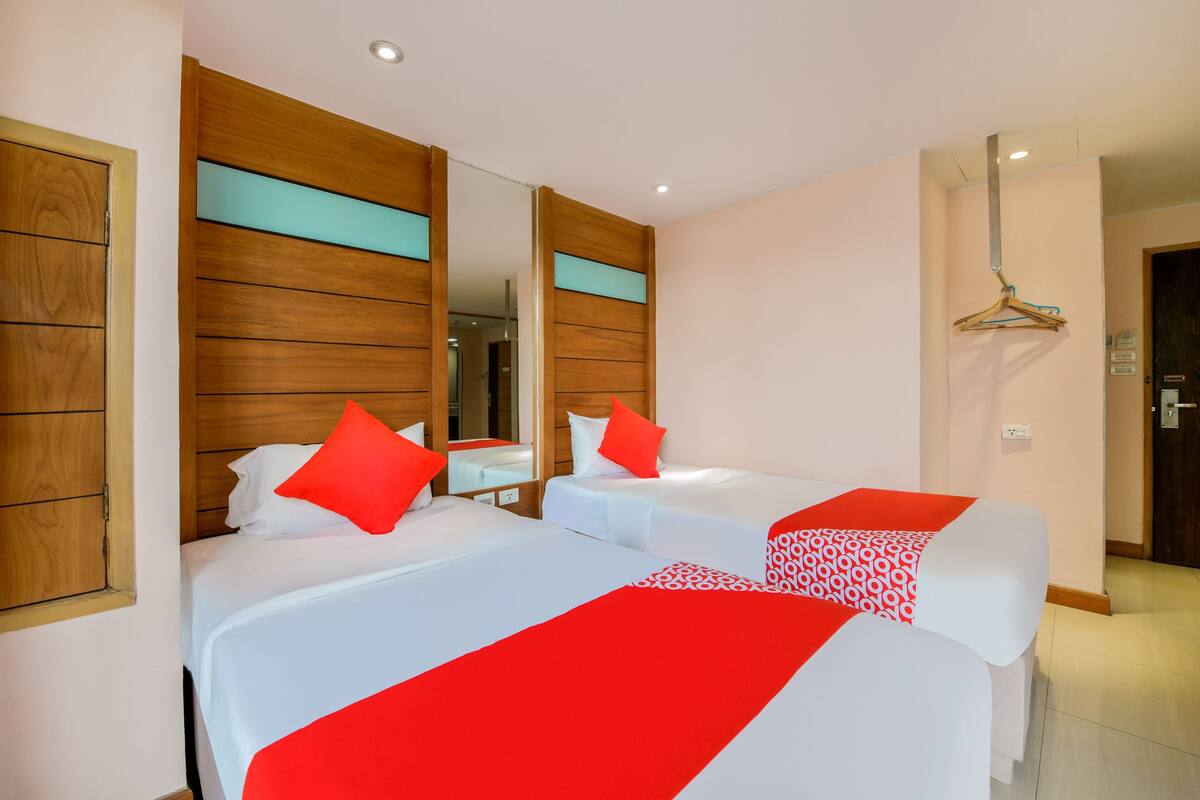 A hotel room with two beds, wooden paneling on the walls, a mirror, and a hanging coat rack.